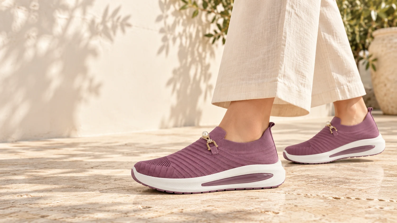 Mauve pearl-accent knit slip-ons worn with cream linen trousers on a sunlit terrace, photographed below the knees